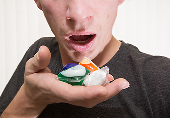 A man holding laundry detergent pods close to his open mouth.