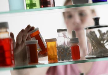 Woman looking at bottles of medications in a cabinet, addressing the opioid crisis with safe disposal