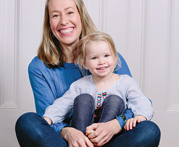 Samantha Dabney survived a stroke. She is sitting and smiling while holding her daughter in her lap, who is also smiling.