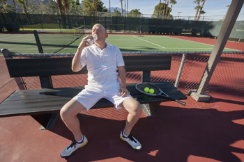 Senior male tennis player drinking water while relaxing on court