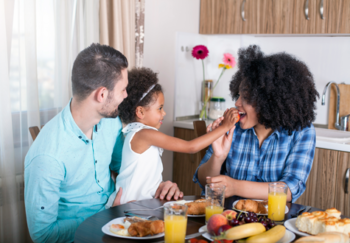 Child feeding parents fruit at the breakfast table
