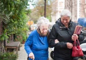 woman helping aging relative walk down the sidewalk