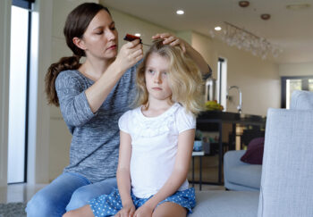 A woman and child sitting on a couch while the woman combs the child's hair
