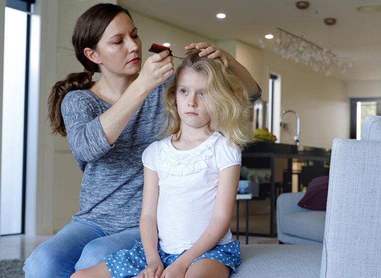 A woman and child sitting on a couch while the woman combs the child's hair