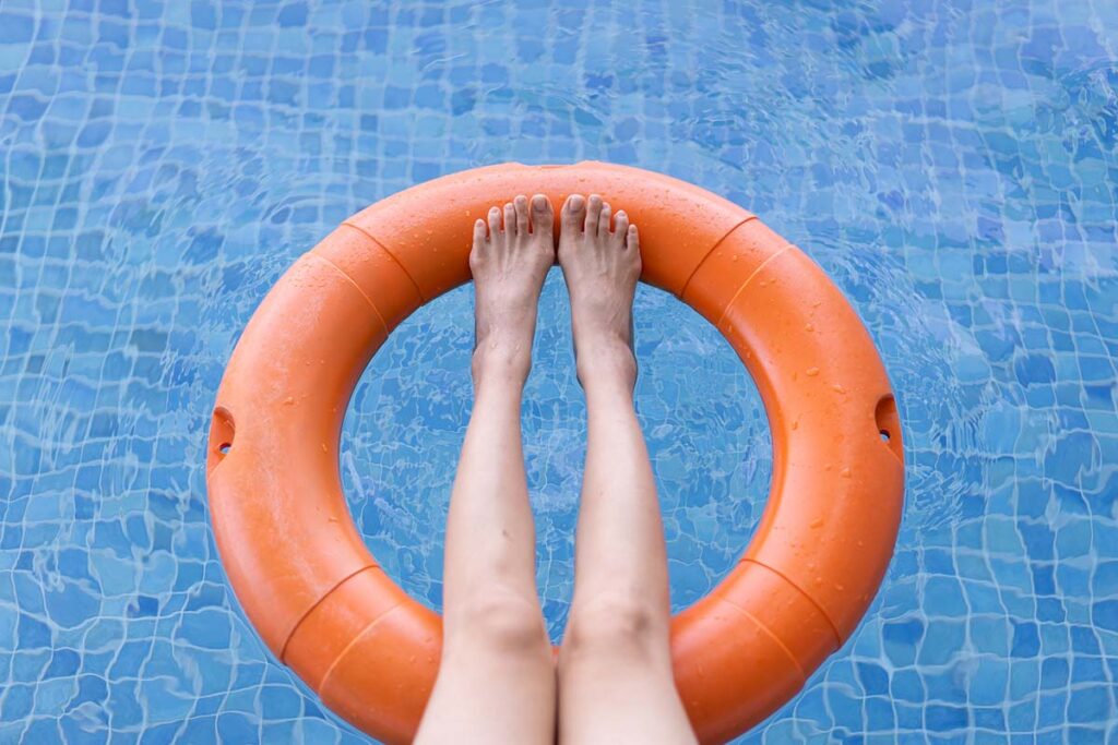 Asian lady's leg resting against a floating lifebuoy on the surface of a swimming pool