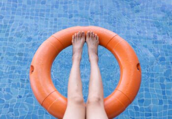 Asian lady's leg resting against a floating lifebuoy on the surface of a swimming pool