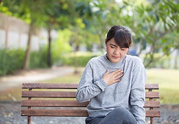 A woman sitting on a bench and touching her chest where she is experiencing heartburn.