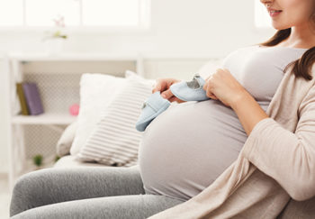 woman pregnant holding baby shoes