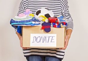 Woman hand holding donation box with clothes, toys and books.