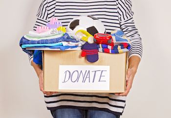 Woman hand holding donation box with clothes, toys and books.