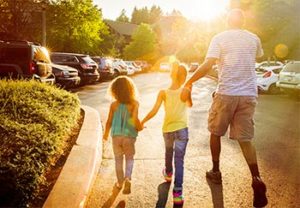 Man holding hands with two small daughters walking through the parking lot