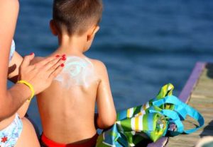 A mother applying sunscreen on to her son's back at the beach.
