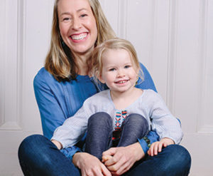 Samantha Dabney sitting and smiling while holding her daughter in her lap, who is also smiling.