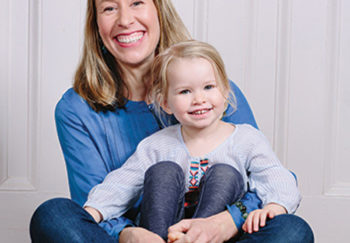 Samantha Dabney sitting and smiling while holding her daughter in her lap, who is also smiling.