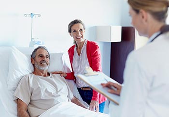 man lying in hospital bed with a woman standing beside him and doctor facing him