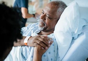 man lying in hospital bed with a woman standing beside him and doctor facing him