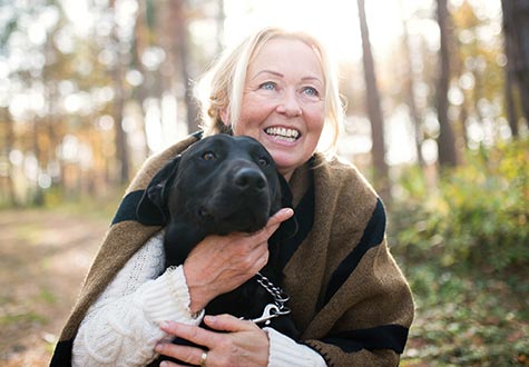 smiling woman in the woods, hugging a black lab dog