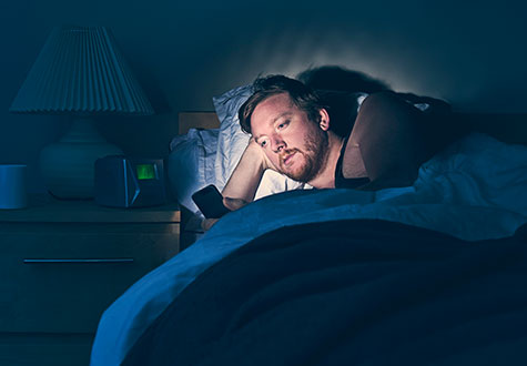 man lying in bed looking at glowing cell phone