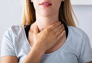 woman touching the base of her neck, where the thyroid is