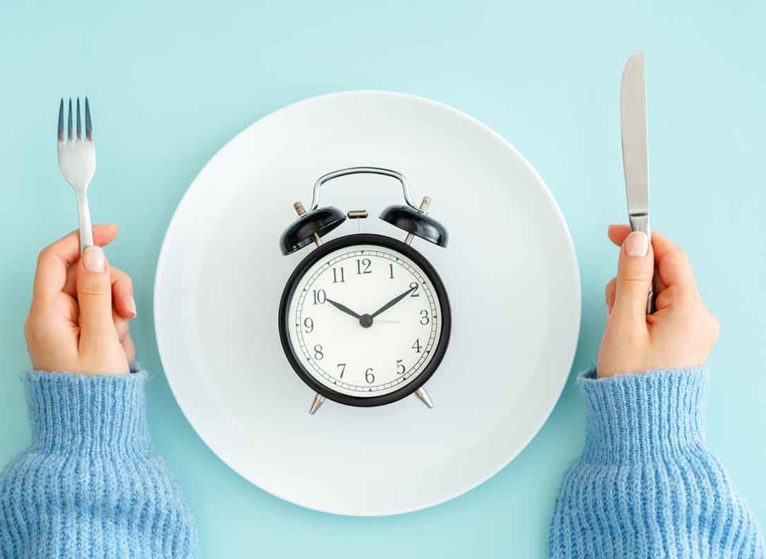 a clock on a plate with a person holding fork and knife