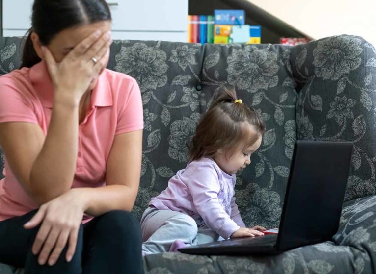 toddler banging on laptop while parent buries head in hands