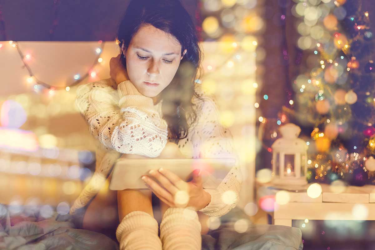 person sitting near Christmas tree, looking at a tablet