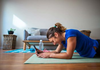 person lying on yoga mat, smiling and looking at tablet