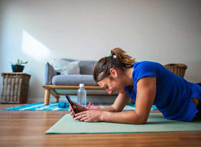 person lying on yoga mat, smiling and looking at tablet