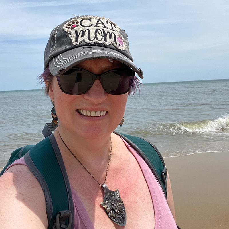 Charity at the beach, facing the camera, wearing "Cat Mom" hat and pink shirt