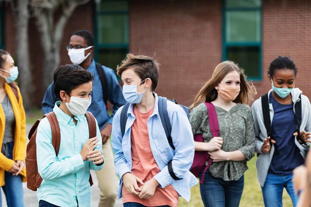 several middle school kids wearing a mask and walking outdoors