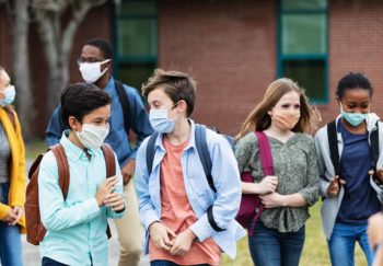 several middle school kids wearing a mask and walking outdoors