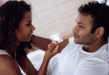 two people close together looking at each other; one is holding a condom