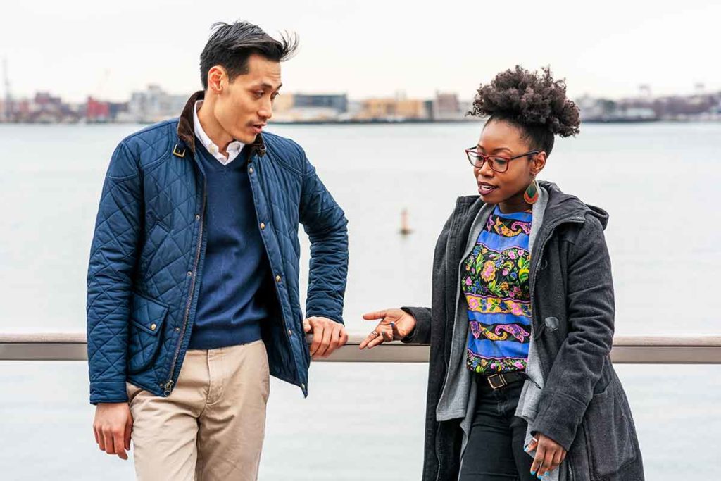 A man and a woman standing by a railing in front of water discussing things not to say to someone with a chronic illness.