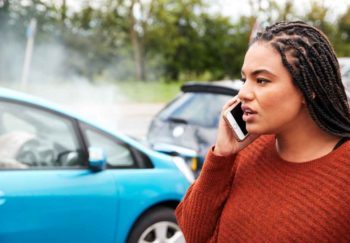 A young woman is on the phone with following a fender bender between two cars