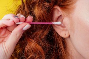 woman holds Q-tip close to ear