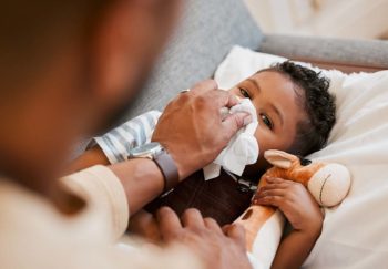 father blows a child's nose before giving him children's medicine