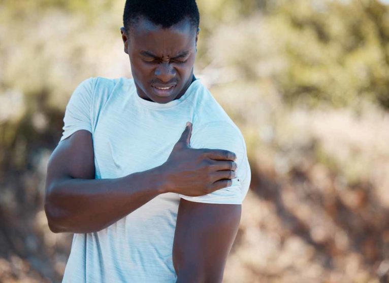 A black man holding his left shoulder after suffering a stinger