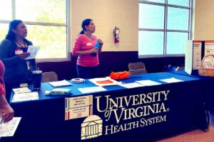 Two women at a UVA Latino Health Initiative table at a health fair. They're helping to reduce heart disease disparities by recruiting more Latinos into clinical trials.