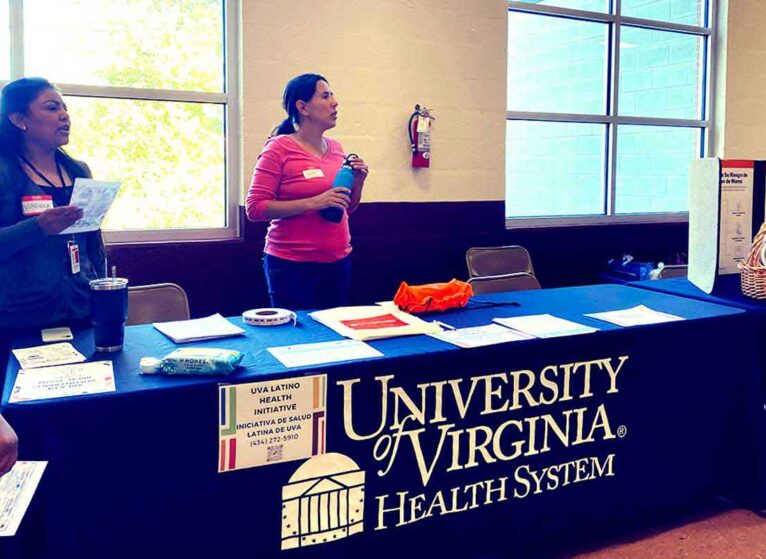 Two women at a UVA Latino Health Initiative table at a health fair. They're helping to reduce heart disease disparities by recruiting more Latinos into clinical trials.