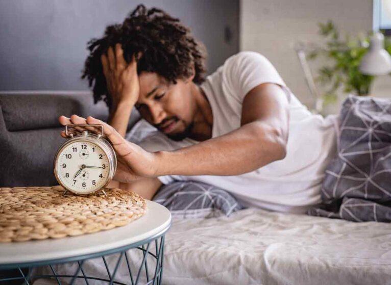 A man waking up, reaching out to stop an alarm clock