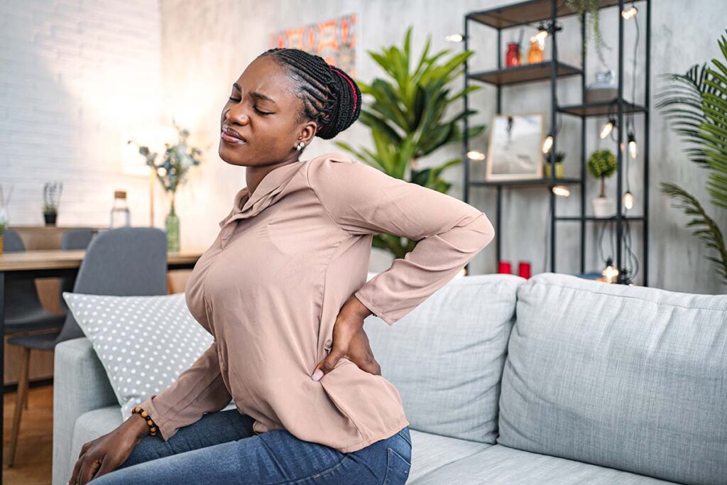 Woman suffering with back pain while sitting at home