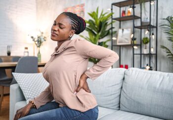 Black woman suffering with back pain while sitting at home