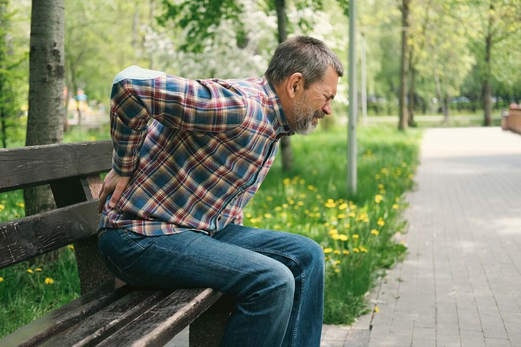 Man sitting on bench holding his hand to his lower back in pain