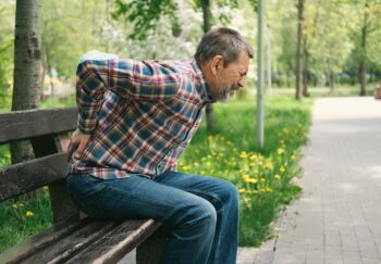 Man sitting on bench holding his hand to his lower back in pain