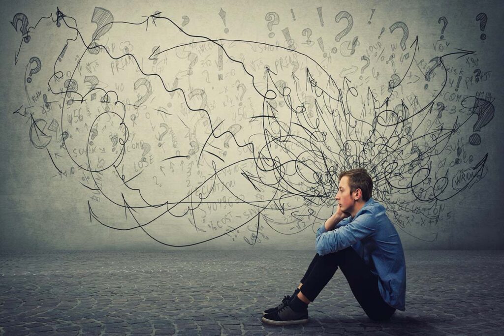 Boy sits on floor, with lines and question marks on wall behind him.