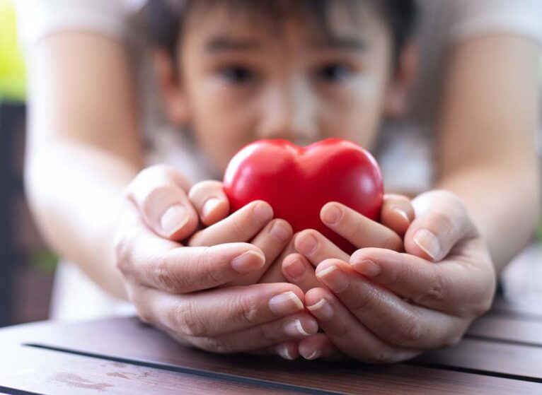 Parent's and child's hands both hold a heart