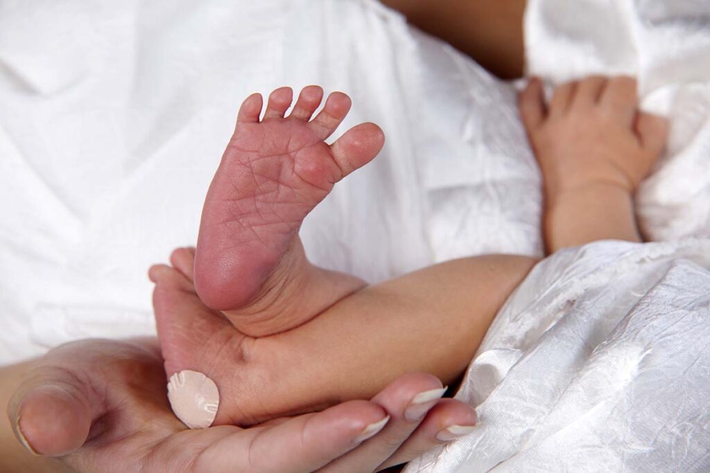 Loving mom holds newborn feet, with bandaid from heel stick