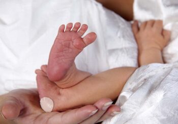 Loving mom holds newborn feet, with bandaid from heel stick
