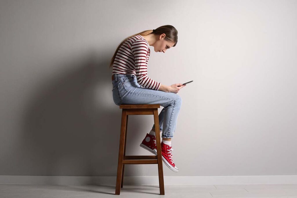 Girl bent over looking at phone while sitting on stool