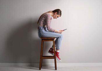 Girl bent over looking at phone while sitting on stool